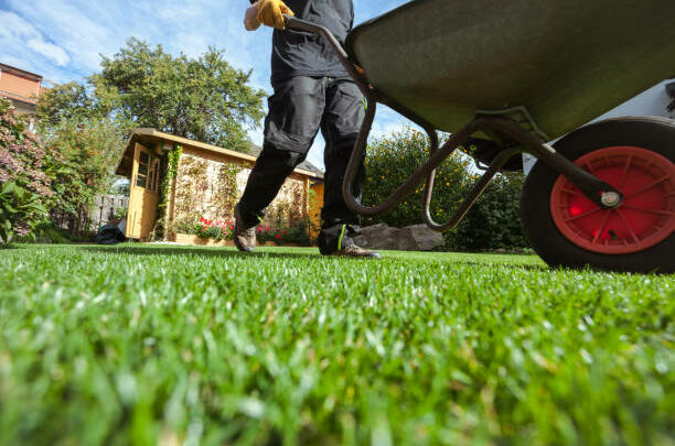 Man pushing wheelbarrow over green grass in backyard; low angle view; obscured face; real people;